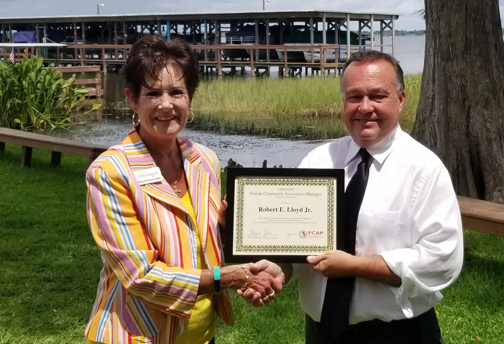 A man and woman holding an award in front of a body of water.